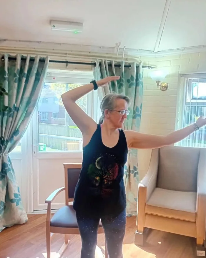 Anne Berry demonstrating a gentle standing movement during an exercise session