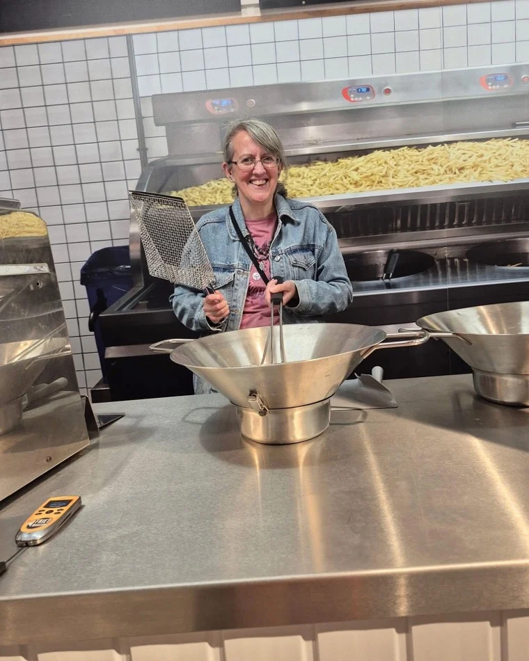 Anne laughing while having a go behind a chip-shop fryer on her travels