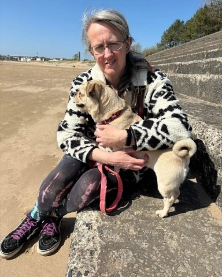 Anne sitting on the beach in the sunshine giving her dog a cuddle