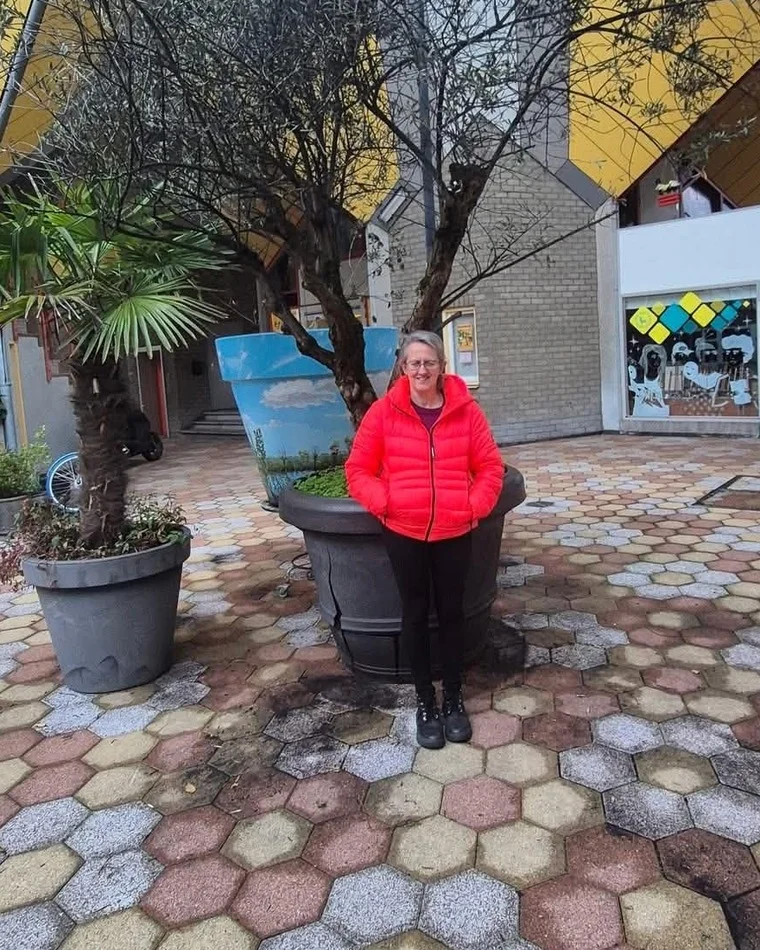 Anne smiling outdoors while travelling, in a bright courtyard