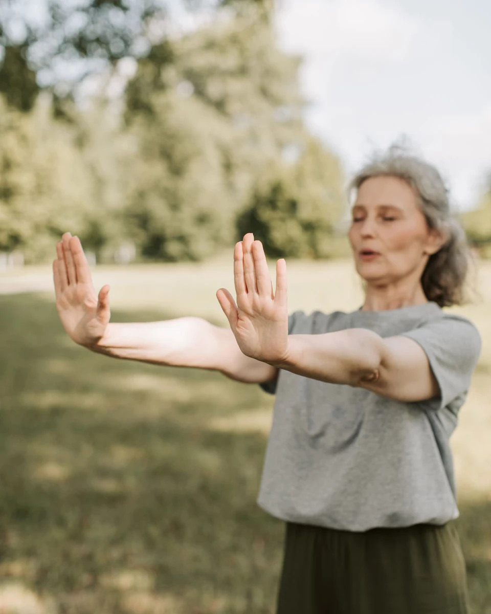 An older woman practising calm, gentle Tai Chi movements outdoors