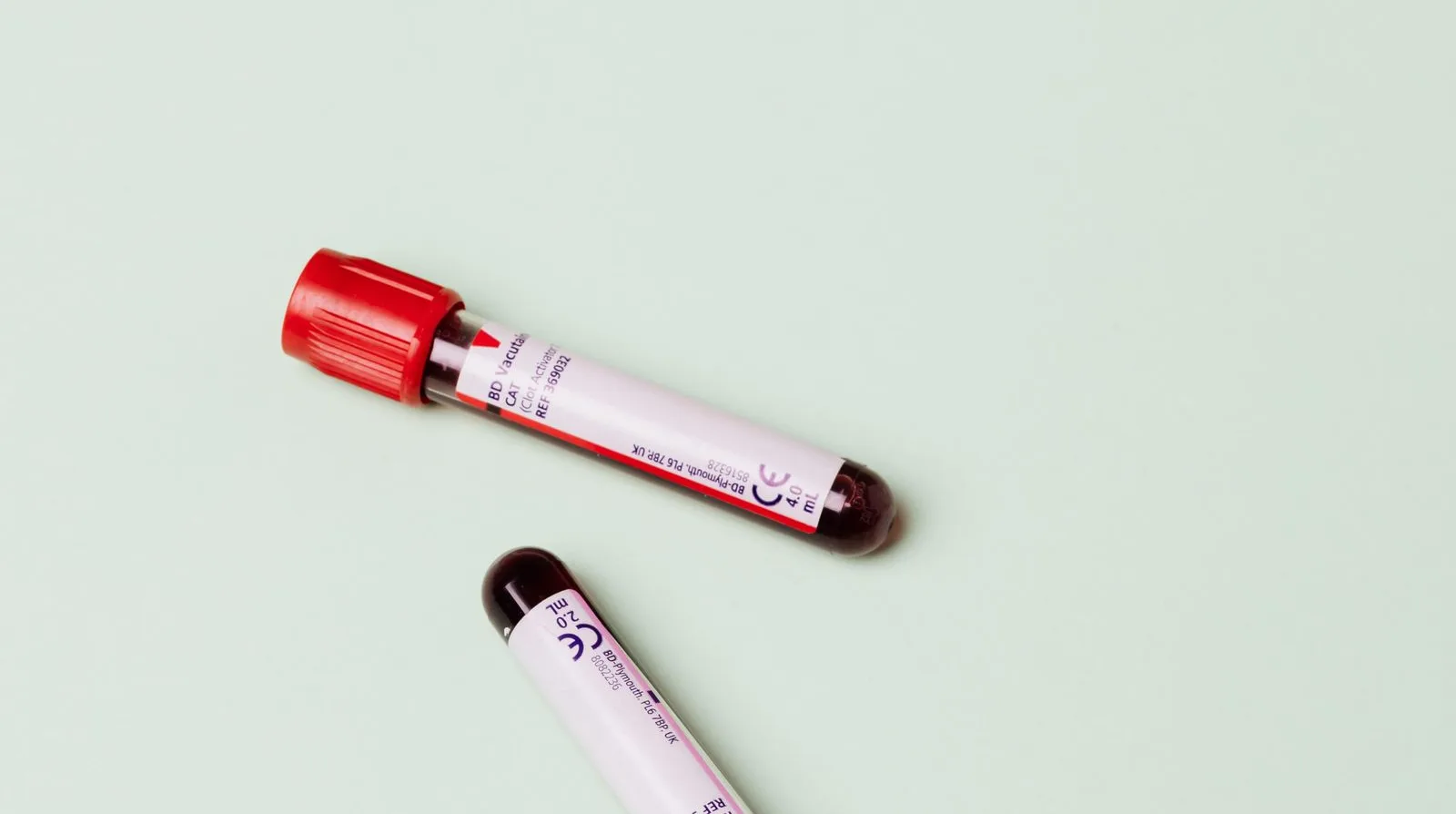 Two clean blood sample tubes resting on a calm, soft-green surface — private phlebotomy and analysis